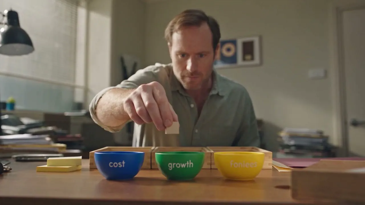 A hand moving a plain timber block between bowls on the meeting table