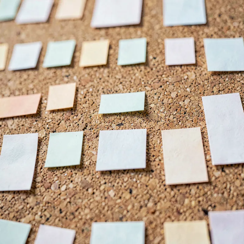 A cork board with small blank coloured cards pinned in an even grid