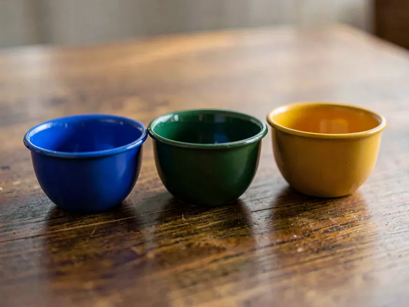 Three empty enamel bowls in cobalt blue, deep green and ochre, in a row on a timber desk