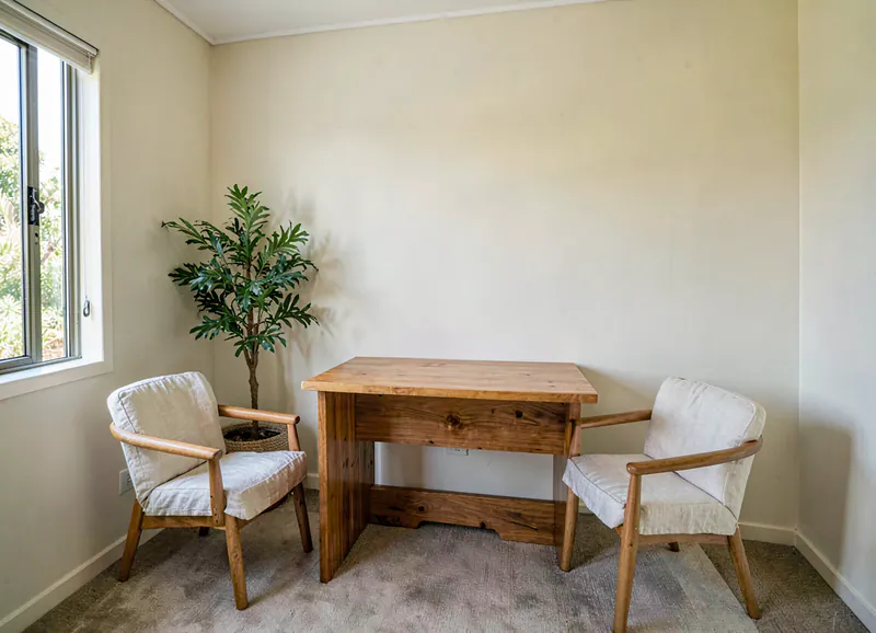 The front room of the practice, a plain timber desk, two linen chairs and morning light